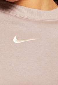 Ljusrosa sweatshirt med ribbad halsringning, som har en liten, krämfärgad broderad Nike-logga på bröstet. Mjuk tygkänsla.
