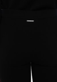 Pantaloni neri realizzati in tessuto elastico, con un design aderente e una piccola etichetta con logo argentato sulla cintura posteriore. Texture liscia su tutta la superficie.