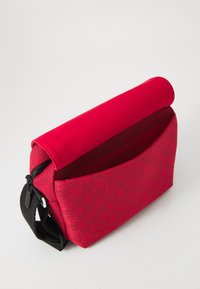 Borsa a tracolla rossa con motivo texturizzato, chiusura con zip e soffice pattina. Presenta una tracolla nera e una tasca interna per l'organizzazione.