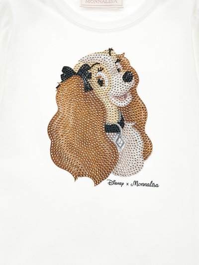 T-shirt bianco con un design di un cane cartone animato, arricchito con strass multicolori. Il tessuto appare liscio e leggero.