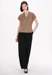 Top marrone a maniche corte e scollo a V abbinato a pantaloni neri a gamba larga. Tessuto liscio con una sottile lucentezza. Silhouette classica con dettagli minimi.
