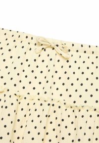 Tela crema con lunares negros, cintura elástica con lazo y detalle de costura fruncida.