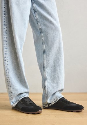 Baskets noires en suède texturé et maille, avec un bout arrondi et une semelle en caoutchouc, associées à un jean en denim bleu clair, ample.
