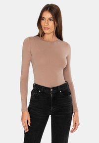 Pitkähihaista, hyvin istuvaa ykköstä pehmeästä, vaaleanruskeasta kankaasta, yhdistettynä korkeavyötäröisiin mustiin farkkuihin, joissa on etutaskut ja nappikiinnitys.