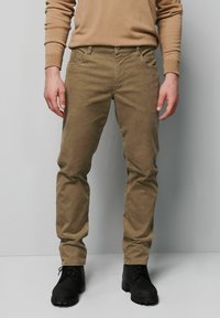 Beżowe spodnie sztruksowe z pięcioma kieszeniami, prostym krojem i subtelną fakturą. Noszone z czarnymi butami sznurowanymi.