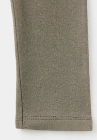 Gros plan d'une manche en tissu vert olive avec des coutures apparentes le long des bords et un ourlet replié en bas.