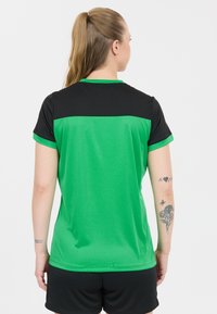 Grön och svart sporttröja, kortärmad, med en slät textur och kontrasterande färgblock. Bärs med svarta shorts.