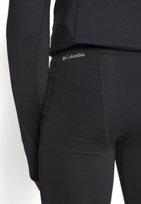 Czarne legginsy sportowe wykonane z gładkiego, elastycznego materiału. Cechy obejmują dopasowany krój oraz małe logo Columbia na pasie.