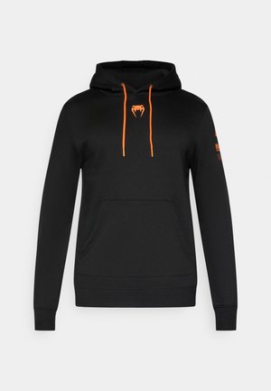 Must kapuutsiga pusa oranžide nööpidega ja ukselaba rinnal, kus on kõbra logo. Omab ees taskut ning soonikkoes mansette ja ääri. Lihtne disain.