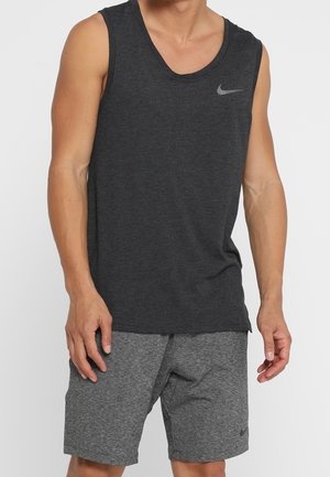 Mand iført mørkegrå ærmeløs Nike-trøje og matchende grå shorts, stående med afslappet kropsholdning mod en ensfarvet baggrund.