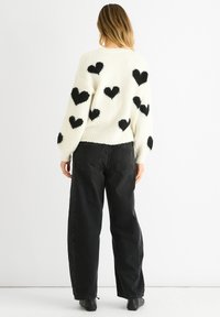 Witte gebreide trui met zwarte hartpatronen, lange mouwen en ribbelboorden. Gecombineerd met hoge taille zwarte denim jeans.