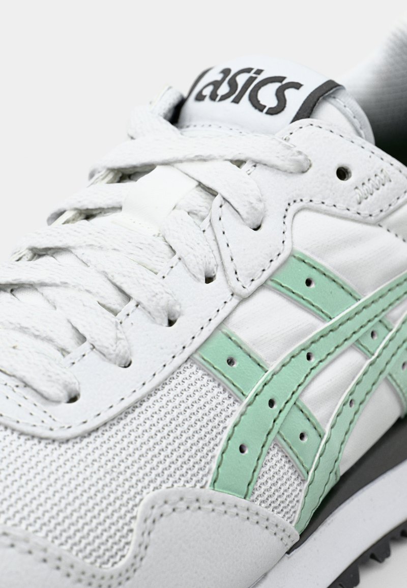 Sneaker bianco con texture in rete e accenti in pelle. Strisce verdi e lacci ben visibili completano il design. Logo sulla linguetta.