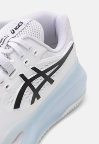Weißer Sportschuh mit Obermaterial aus Netzgewebe, schwarzem Asics-Logo und durchsichtiger hellblauer Sohle. Verfügt über strukturierte Details und Ösen für die Schnürsenkel.