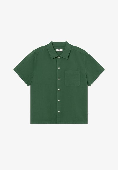 Chemise verte à manches courtes avec col et poche poitrine, ornée d'une petite broderie de logo sur la poche.