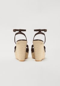 Brown wedge sandals with woven jute platform, ankle strap, glossy leather upper, and textured heel.