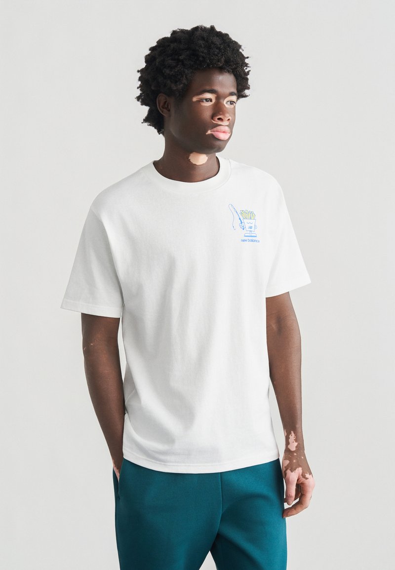 Λευκό βαμβακερό μπλουζάκι με κοντά μανίκια, με μπλε γραφικό σχέδιο και κείμενο στην αριστερή πλευρά του στήθους. Συνδυασμένο με παντελόνια σε τιρκουάζ αποχρώσεις.