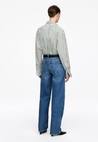 Striped button-up shirt in green and white, paired with high-waisted blue denim jeans. The shirt features long sleeves and a relaxed fit.