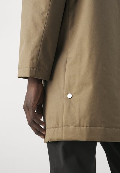 Cappotto khaki realizzato in un tessuto morbido, dal design dritto, con dettagli a scatto laterali e una vestibilità comoda, caratterizzato da cuciture visibili e una texture liscia.