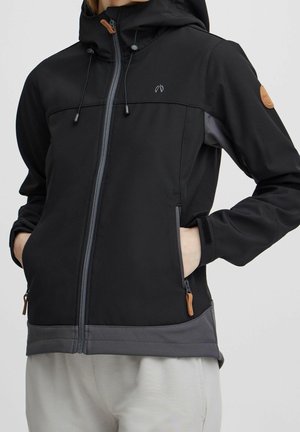 Personne portant une veste à capuche zippée noire et grise, les mains dans les poches zippées avec des tirettes en cuir.