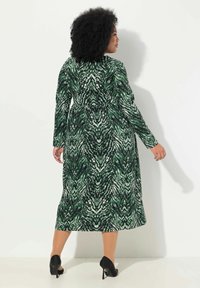 Pitkä vihreä mekko, jossa on kieppuva kuvio, pitkät hihat, istuva vyötärö ja levenevä alaosa. Yhdistettynä mustiin korkokenkiin.