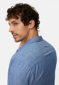 Hellblaues Hemd mit Knopfleiste, weicher Textur und kurzen Ärmeln, mit einer dezenten Rückenpasse und einem Kragen.