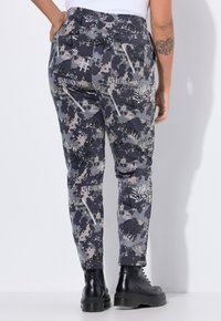 Tætsiddende bukser i et grå og navy camouflage mønster med tekstgrafikker. Fremstillet af et blødt stof med elastisk talje. Sorte kraftige støvler.