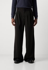 Pantalones de pierna ancha negros con cintura alta, que presentan pliegues frontales y acentos de hardware en los laterales. Tejido suave con un acabado pulido.