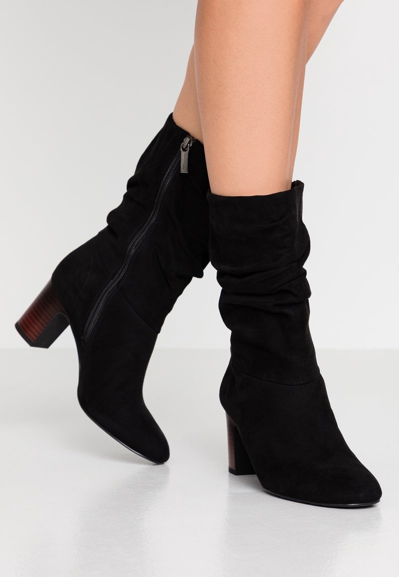 Bottines en suède noir avec un design décontracté, fermeture éclair sur le côté et un large talon en bois ; la texture lisse améliore l'apparence générale.