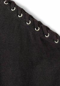 Tissu noir avec des lacets noirs enfilés à travers six œillets métalliques argentés le long d'un bord courbe sur fond blanc.