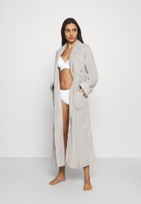 Light grey robe made of soft fabric, featuring a shawl collar, two front pockets, and an embroidered logo on the chest.