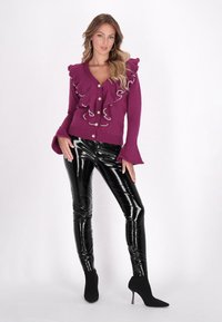 Cardigan de punto morado con detalles en volantes y botones de perlas, combinado conleggings de vinilo negro brillante y botas negras de tacón puntiagudo.