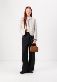 White tweed jacket with black trim, cropped black top, loose black trousers, and brown quilted handbag, set against a neutral background.
