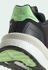 Scarpa sportiva nera con parte superiore testurizzata, accento verde sul tallone e intersuola bianca ammortizzata. Presenta una suola in gomma nera a motivo.