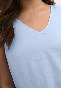 Top sans manches bleu clair en tissu léger avec un décolleté en V et une texture lisse. L'ourlet est simple, sans ornements.