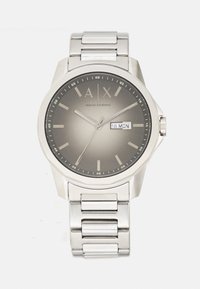 Orologio da polso in metallo argentato con quadrante sfumato grigio, tre lancette, visualizzazione di data e giorno con indicazione "18 LUN" e marchio Armani Exchange.