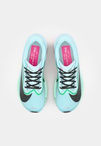 Scarpe da ginnastica azzurre chiare con accenti neri, suola verde, parte superiore in rete e lacci neri. Include etichette rosa all'interno con i dettagli del marchio.
