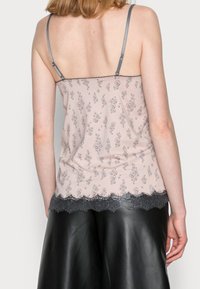 Light pink camisole with gray intricate floral patterns, thin gray straps, and a ruffled black lace hem accentuating the bottom edge.