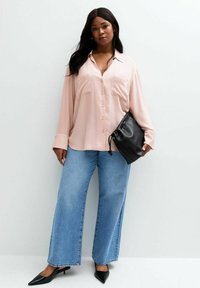 Camicia rosa chiaro con bottoni e due tasche sul petto, abbinata a jeans larghi in denim blu. Una pochette nera e tacchi a punta neri completano il look.