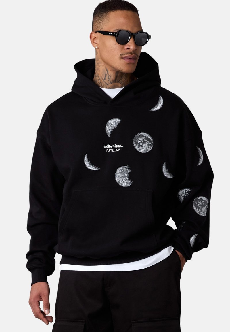 Haut à capuche noir avec une poche avant arborant divers graphiques de lune en blanc et gris. Design à capuche avec des poignets et un ourlet côtelés.
