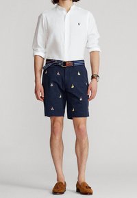 Navyshorts med broderi av flerfärgade segelbåtar, matchade med en vit linneknappskjorta och ett brunt bälte. Bruna loafers fulländar outfiten.