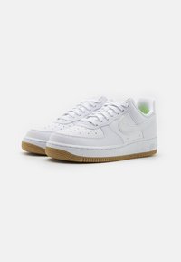 Bílé kožené tenisky s perforovanou špičkou, texturovanou boční částí, zeleným akcentem na obložení a hnědou gumovou podrážkou. Minimalistický design s logem.