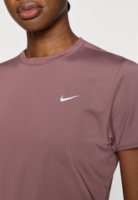 Αθλητικό μπλουζάκι με κοντά μανίκια σε ύφασμα σε χρώμα ξεθωριασμένο ροζ, με στρογγυλή  λαιμόκοψη και μικρό λευκό λογότυπο Nike στο αριστερό στήθος.