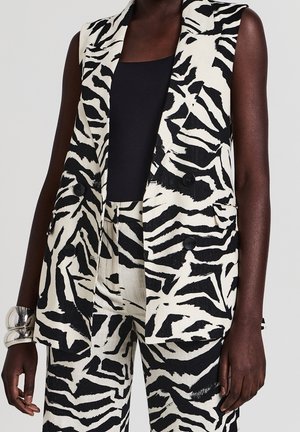 Ärmelloser Blazer mit schwarz-weißem Zebramuster und passende Hose, getragen über einem schwarzen ärmellosen Top, accessoriert mit einem silbernen Armband.