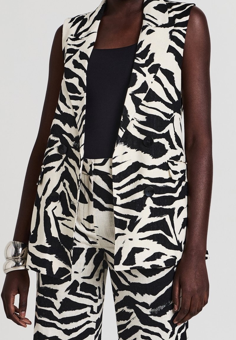 Blazer sans manches imprimé zèbre noir et blanc avec pantalon assorti, porté sur un top noir sans manches, accessoirisé d'un bracelet en argent.