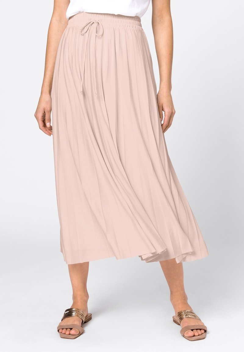 Falda larga plisada de color rosa claro con cintura elástica y cordón ajustable. Combinada con sandalias planas marrón claro con detalles metálicos.