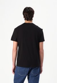 Černé bavlněné tričko s krátkým rukávem, kulatým výstřihem a jednoduchým designem. Nosené s modrými džínami, zobrazené zezadu.