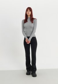 Szürke és fehér csíkos garbó, slim fit fazon, fekete bővülő farmernadrággal és vastag fekete cipőkkel, semleges háttér előtt.