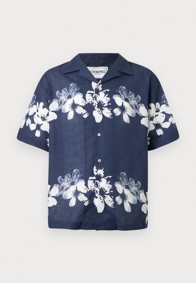 Chemise courte à manches en marine avec imprimé floral blanc, bouton devant, col évasé et tissu léger. Les accents incluent des boutons et une coupe décontractée.