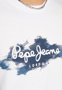 Bílý bavlněný tričko s modrým akvarelovým vzorem a logem "Pepe Jeans London" v písmovém písmu. Klasický kulatý výstřih, volný střih.