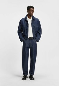 Donkerblauwe denimjack met een klassiek ontwerp en voorzakken. Gecombineerd met bijpassende donkerblauwe loose-fit jeans en zwarte schoenen.
